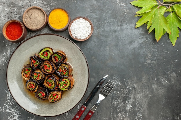 Free photo top view stuffed aubergine rolls hot pepper powder turmeric in small bowls leaves fork and knife on grey surface