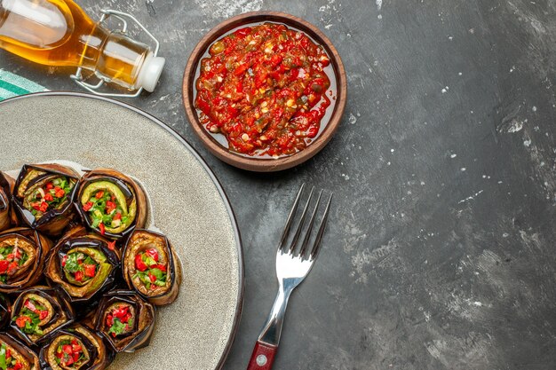 Top view stuffed aubergine rolls in white oval plate fork oil adjika on grey background