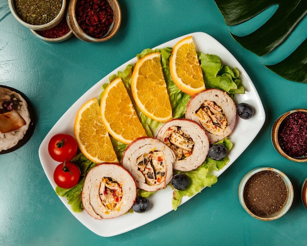 Top view of stuffed chicken rolls with vegetable and herbs served with orange slices and cherry tomatoes on a platter