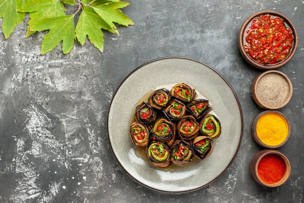 Top view stuffed eggplant rolls in white plate different spices adjika in small bowls on grey surface