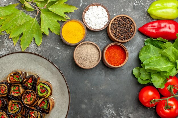 Top view stuffed eggplant rolls in white plate tomatoes peppers aubergines greens different spices on grey background