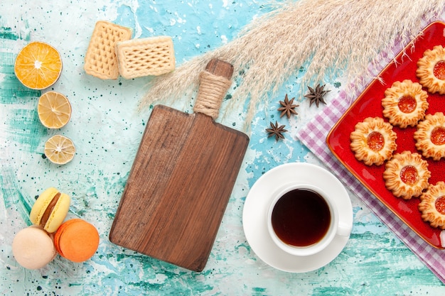 Foto gratuita biscotti di zucchero vista dall'alto all'interno del piatto rosso con una tazza di tè e macarons su sfondo blu