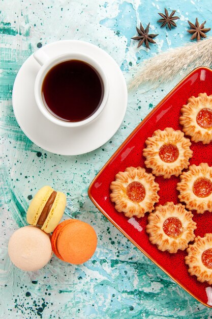 Top view sugar cookies with cup of tea and macarons on the blue background