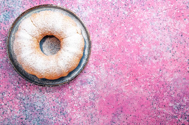 Top view of sugar powdered cake round formed on light-pink surface