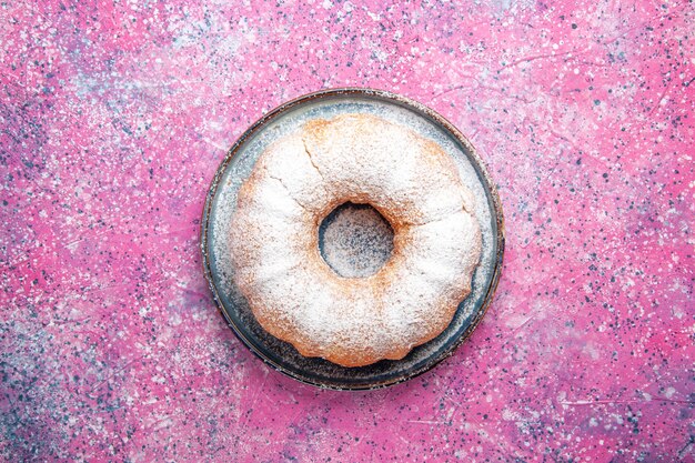 Top view of sugar powdered cake round formed on pink surface