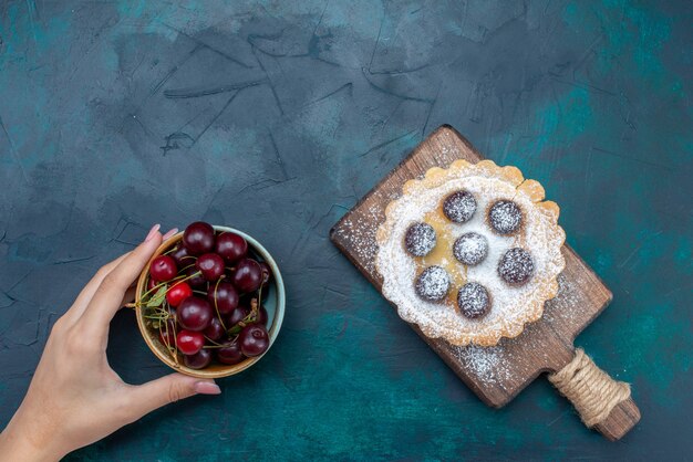 Вид сверху сахарной пудры с вишней внутри и вместе со свежей вишней на темно-синем фоне фруктовый торт бисквитный сладкий