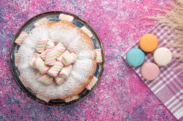 Top view of sugar powdered cake with french macarons on pink surface