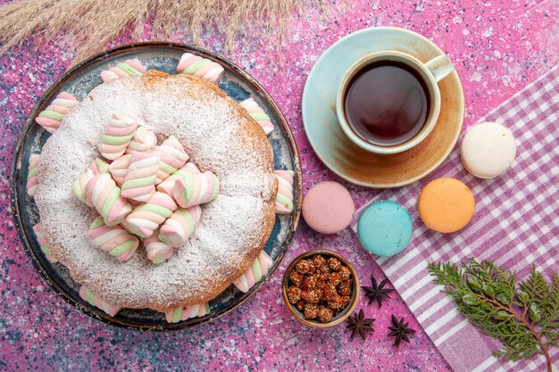 Top view of sugar powdered cake with marshmallows and cup of tea on pink surface