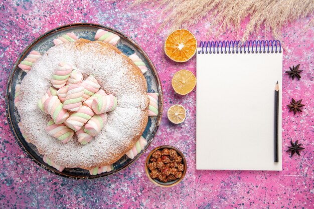 분홍색 표면에 달콤한 마시멜로와 메모장 설탕 가루 케이크의 상위 뷰
