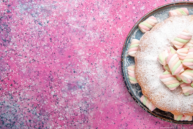 Top view of sugar powdered cake with sweet marshmallows on pink surface