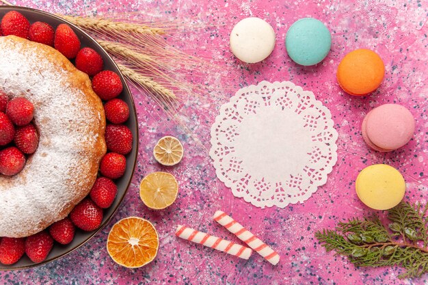 Вид сверху клубничный пирог с сахарной пудрой и французскими макаронами на розовом