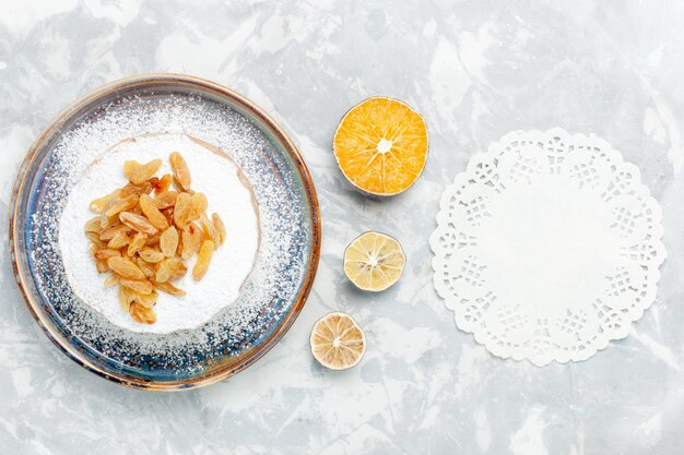 Top view sugar powdered raisins dried grapes on top of little cake inside plate on white desk