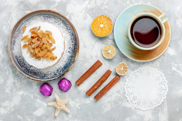 Top view sugar powdered raisins dried grapes on top of little cake with tea and cinnamon on white desk