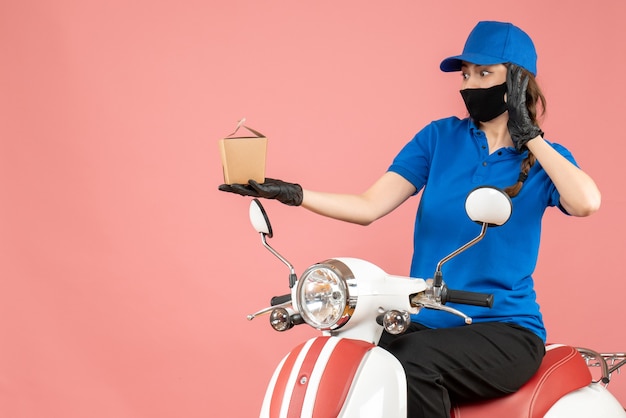 Foto gratuita vista dall'alto del fattorino sorpreso che indossa maschera medica e guanti seduto su uno scooter che consegna ordini su pesca pastello