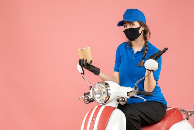 Top view of surprised female courier wearing medical mask and gloves sitting on scooter delivering orders on pastel peach