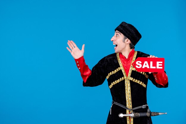 Top view of surprised young man in traditional dress showing sale icon and pointing up on the right side on blue wave background