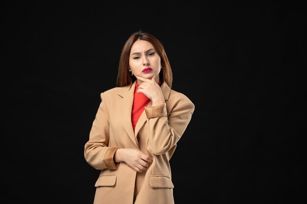 Top view of surprised young woman in a light brown suit in deep thoughts on dark