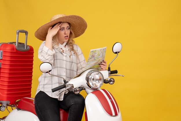 Top view of surprised young woman wearing hat and sitting on motorcycle and concentrated on map on yellow 