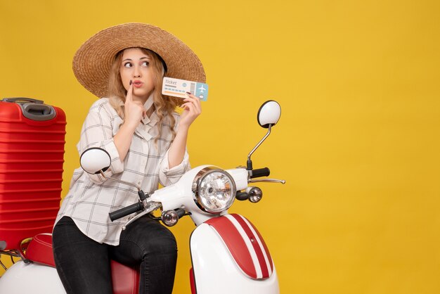 Top view of surprised young woman wearing hat and sitting on motorcycle and holding ticket on yellow 