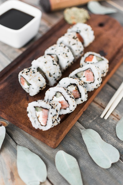 Top view of sushi roll on wooden tray with soya sauce and chopsticks
