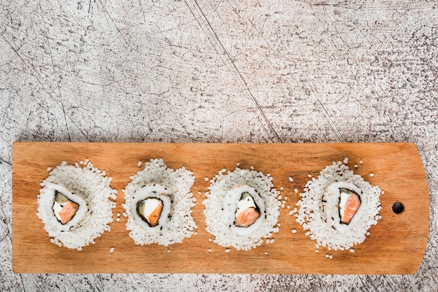 Top view of sushi rolls on white uncooked rice over the wooden tray against grunge background