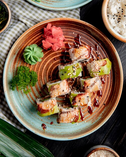 Top view of sushi rolls with eel avocado and cucumber with ginger and wasabi on a plate on wood