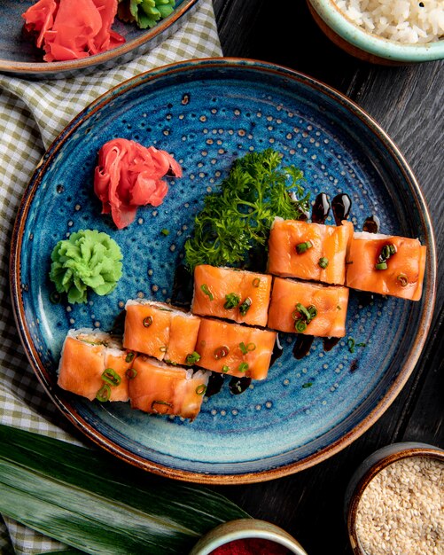 Вид сверху суши роллы с лососем и авокадо и сливочным сыром на тарелку с имбирем и васаби