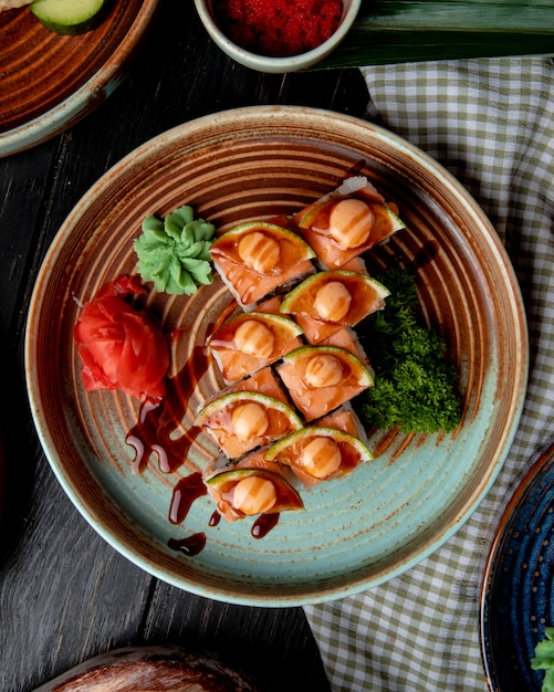 Top view of sushi rolls with shrimps avocado and cream cheese served with ginger and wasabi on a plate on wood