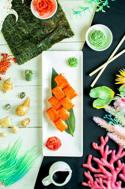 Top view of sushi set rolls with crab meat cream cheese and avocado in caviar of flying fish with soy sauce on bamboo leaf