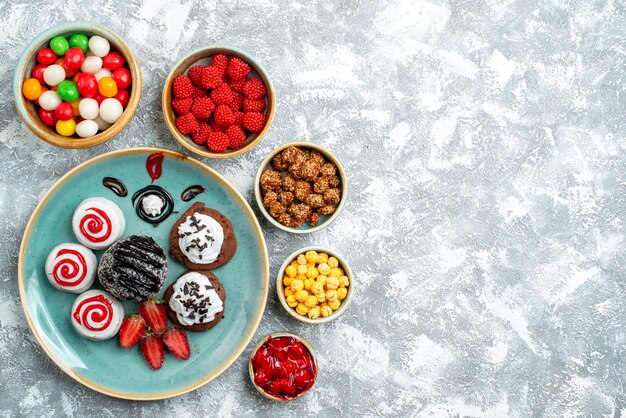 Foto gratuita vista dall'alto biscotti dolci con torta al cioccolato e caramelle sulla scrivania bianca zucchero candito torta biscotto tè dolce