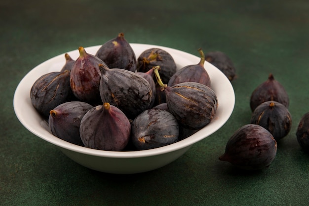 Top view of sweet black mission figs on a bowl on a green wall