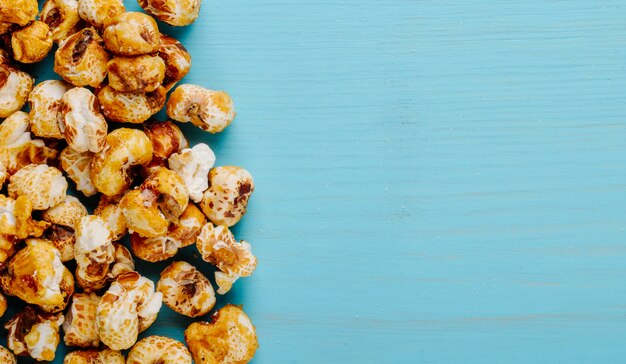 Top view of sweet caramel popcorn scattered on blue background with copy space