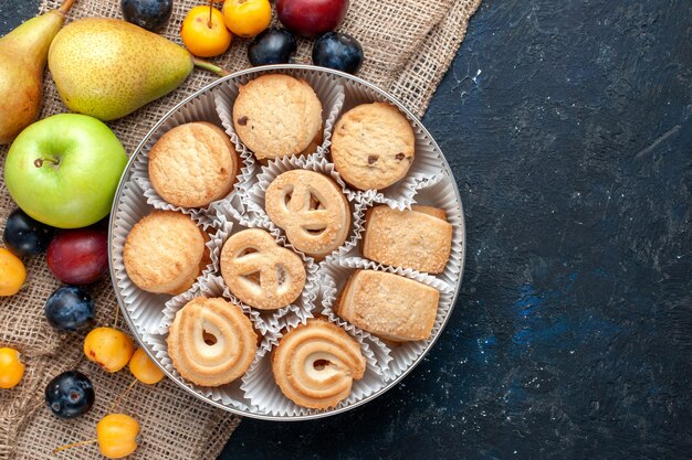 Top view sweet cookies along with different fresh fruits on the dark-blue desk fruit cookie biscuit sweet fresh