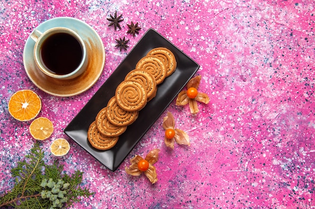 Вид сверху сладкого печенья внутри черной формы с чашкой чая на светло-розовой поверхности
