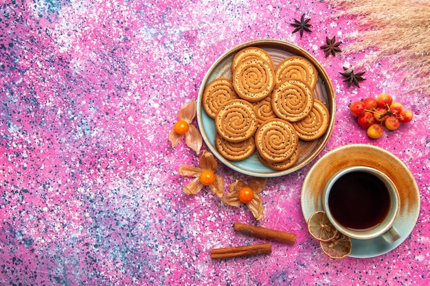 Top view of sweet cookies inside plate with cup of tea on pink surface
