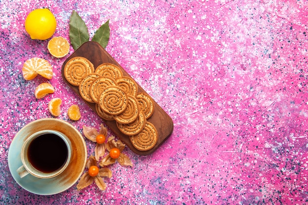 Top view of sweet cookies with cup of tea and citruses on pink surface