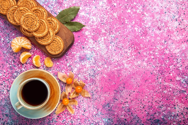 Вид сверху сладкого печенья с чашкой чая и мандаринами на розовой поверхности