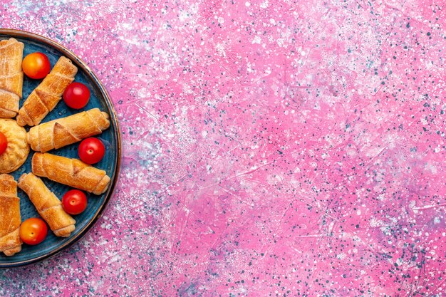 ライトピンクの机の上のプラムとトレイの内側の上面図甘いおいしいベーグル焼きペストリー