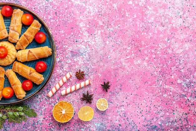 Вид сверху сладкие вкусные рогалики внутри подноса со сливами на светло-розовом столе