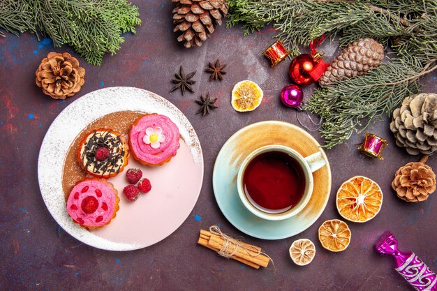 Top view of sweet delicious cakes with fruits and cup of tea on black