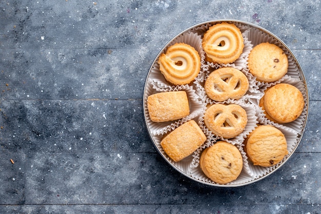 Top view sweet delicious cookies different formed inside round package on the grey desk sweet cake biscuit cookie