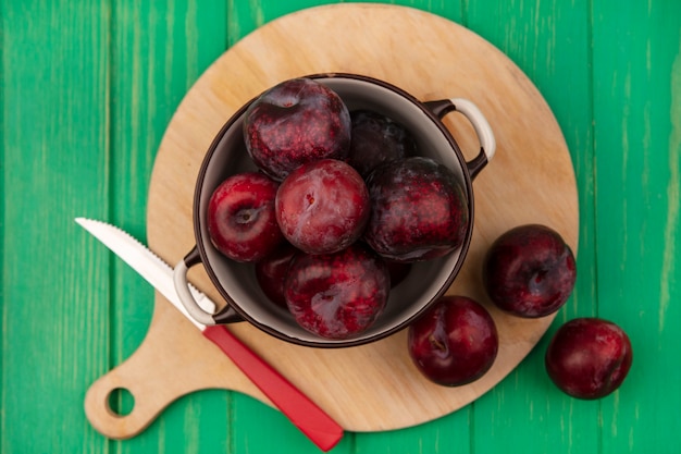 Top view of sweet fresh pluots on a bowl on a wooden kitchen board with knife on a green wooden wall