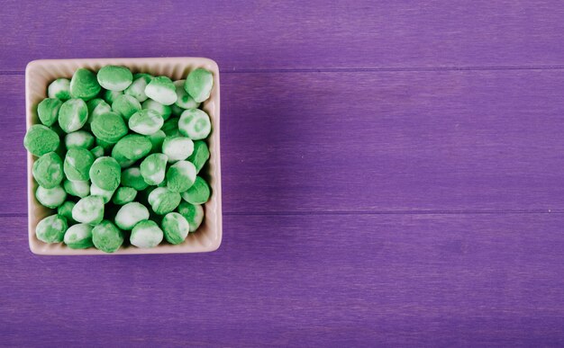 Вид сверху сладкие зеленые конфеты в миску на фиолетовом фоне деревянных с копией пространства