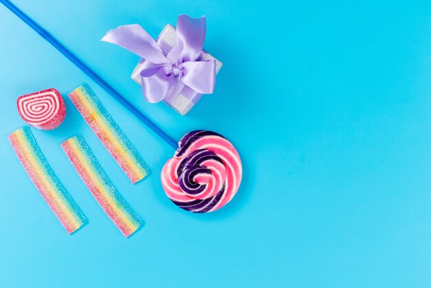 A top view sweet lollipop with blue stick and little purple gift box on blue desk, sweet sugar birthday