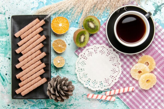 青い机の上にお茶と乾燥パイナップルリングとトップビューの甘い長いクッキー