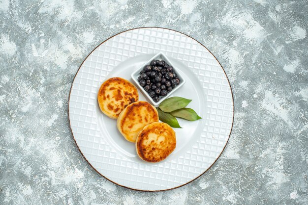 Top view of sweet muffins with berries inside plate on light surface