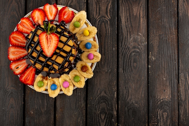 top view sweet pancakes yummy delicious along with sliced red strawberries and bananas inside white plate on the brown wooden background