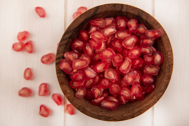 Top view of sweet pomegranate seeds on a wooden bowl with seeds isolated on a white wooden wall