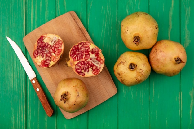 Top view of sweet pomegranates on a wooden kitchen board with knife with pomegranates isolated on a green wooden wall