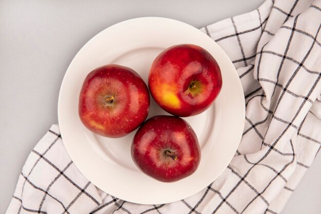 Top view of sweet red apples on a plate on a checked cloth on a white wall